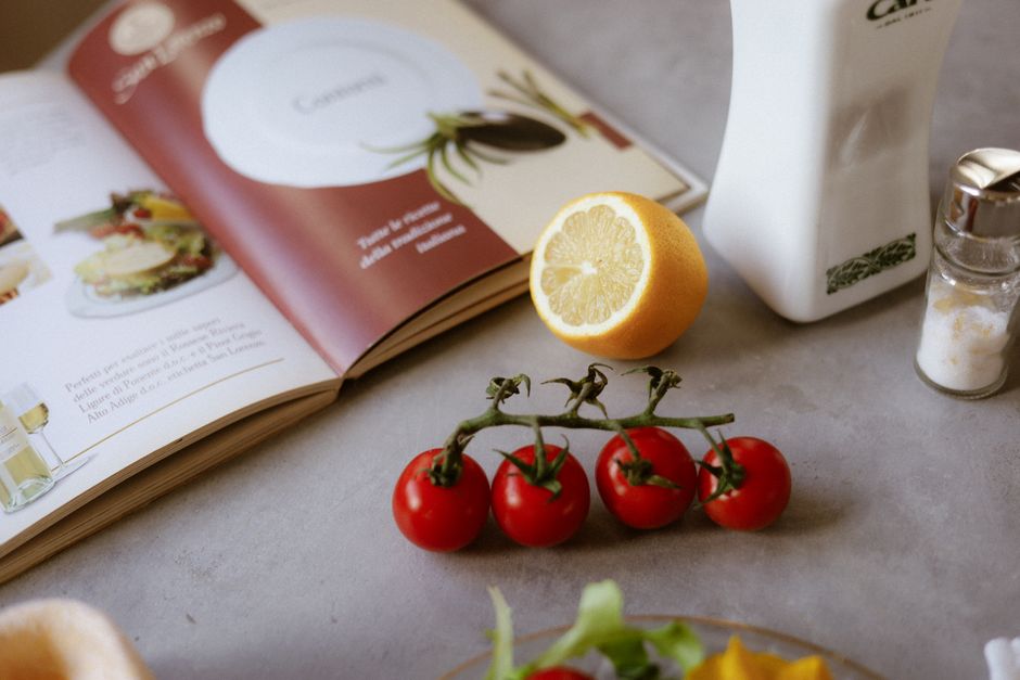 Flat lay of cooking ingredients including tomatoes and a lemon with a cookbook.
