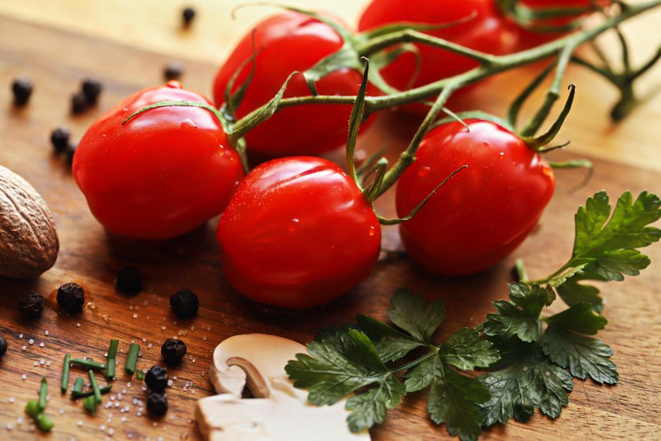 Close-up of fresh cherry tomatoes with herbs and spices on a wooden cutting board.